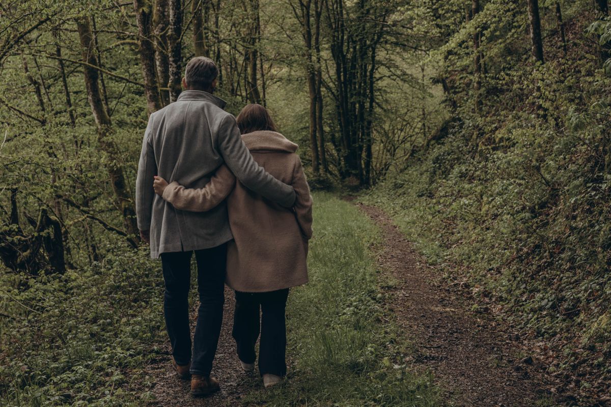 Olga und Markus gehen Arm in Arm einen Waldweg entlang